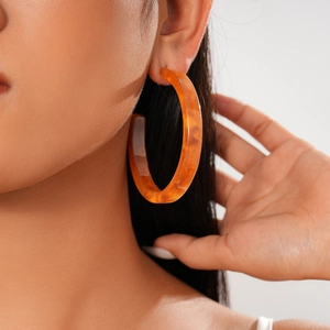 Close-up of a large amber acrylic C-shaped earring with tortoiseshell texture on a model