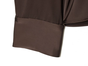 Détail du poignet d'une chemise en satin marron foncé montrant les coutures précises