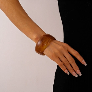 Macro shot of thick amber resin bangle with a smooth polished finish on a model's wrist