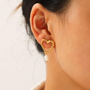 Gros plan sur la boucle d'oreille cœur martelée dorée avec perle blanche sur un modèle