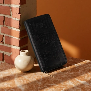Detail view of black dollar bill embossed wallet leaning against a rustic brick wall