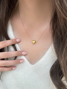 Close-up of a 3D polished gold heart pendant necklace on a soft white sweater