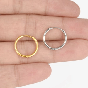 Detail shot of gold and silver irregular spring hoop earrings held by hand for size scale