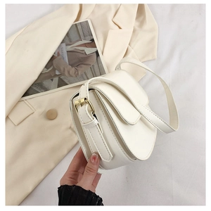 Detail of white leather saddle bag showing flap closure and gold buckle on shoulder strap