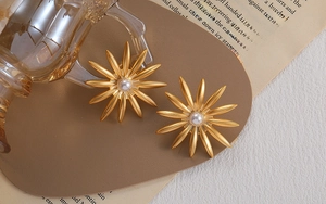 Macro view of golden flower petal earrings with a white pearl on a vintage book