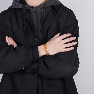 Detailed view of wide golden Cuban link chain bracelet worn on a wrist with black hoodie