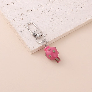 Cute pink dragon fruit keychain with green seeds and silver metal ring on beige stone