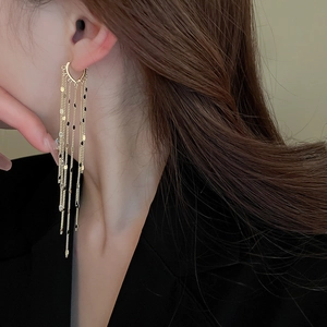 Close-up of long gold fringe earrings with sequins worn by a model in black attire