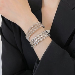Detail of silver triple-layered beaded chain and woven metal bracelet set on wrist