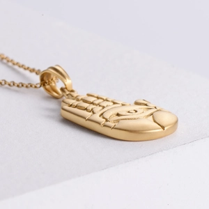 Detail of 18K gold Hamsa Hand pendant necklace with central eye motif on white surface