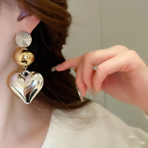 Close-up of stylish round stud and large mirror-finish silver heart pendant earring