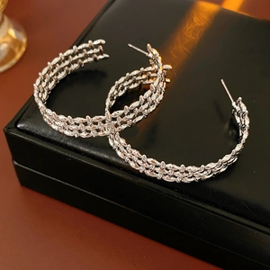 Macro shot of silver-tone C-shape woven earrings on a black leather jewelry box