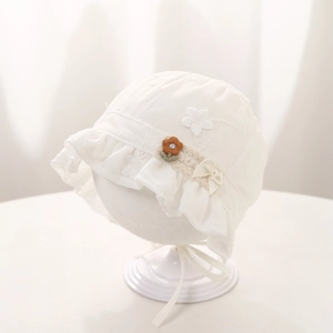 Detailed close-up of white baby lace hat with floral embroidery and pearl ribbon bow