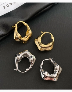 Détail de boucles d'oreilles créoles ondulées en or et argent sur cuir noir élégant