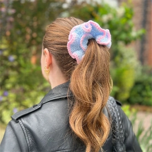 Detailed knit of a ruffled pastel blue and pink scrunchie shown on a ponytail
