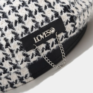 Detail of houndstooth beret featuring a black leather label with LOVES metal chain