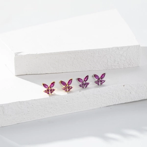 Macro shot of butterfly stud earrings with pink zircon on white stone pedestal