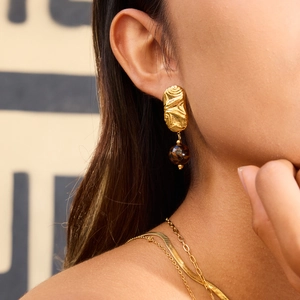 Boucles d'oreilles élégantes en métal doré texturé avec perle marbrée brune sur modèle