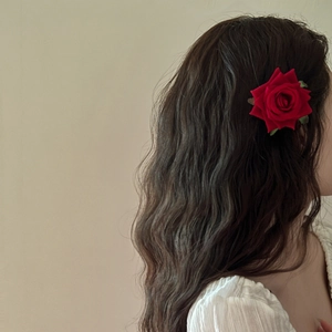 Detail of a large red velvet rose hair clip with green leaves worn on long wavy hair