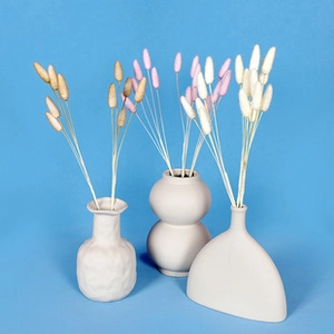 Three white ceramic vases with beige, pink, and white dried pampas grass on blue background