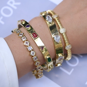 Detail of stacked gold bangles with white zircon and colorful gemstones on a model hand