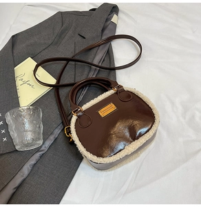Detalle de un bolso de cuero marrón con ribete de piel sintética y placa de metal dorada
