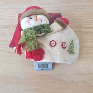 Detail of Christmas snowman plush gift bag on scale showing 101g weight and red fabric texture