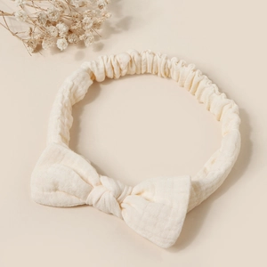 Detailed texture of cream cotton bow headband with elastic band and dried flowers background