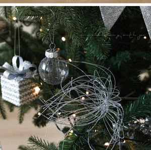 Close-up of silver glitter gift box ornament and glass ball hanging on a Christmas tree