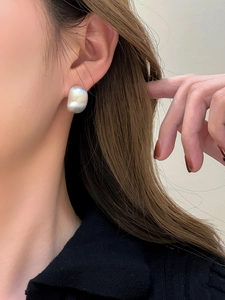Close-up of a silver geometric oval earring with brushed metal texture on a female ear