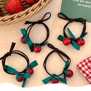 Detail of four handmade cherry hair ties with green bows on a rustic wooden table