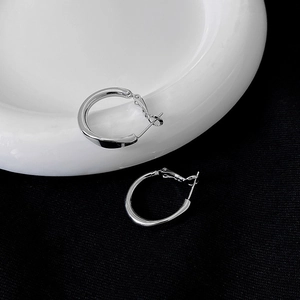 Macro shot of silver geometric earrings with irregular metal hoops on a ceramic tray