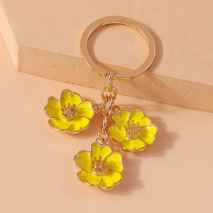 Detail of gold keychain with three yellow enamel peach blossom flower charms on beige background