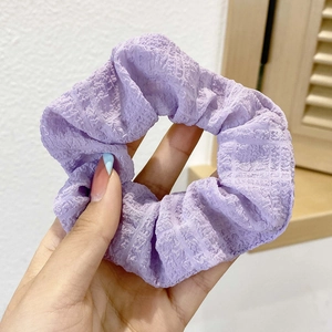 Detail of purple ruched oversized scrunchie hair tie held against a minimalist background