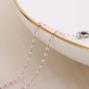 Macro detail of pink translucent beads on a silver chain over a white ceramic plate