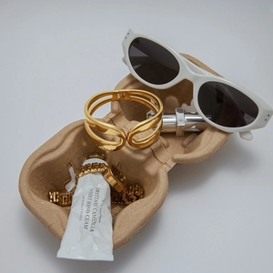 Detail of a hollow gold wide cuff bracelet next to a chain watch on a brown paper tray