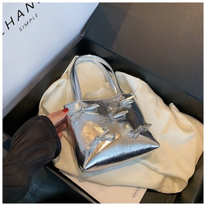 Silver glossy handbag with bow details inside a black gift box on white cloth