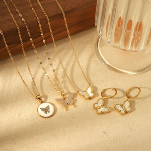 Golden butterfly jewelry set with white shell inlay and rhinestones on beige linen background