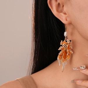 Close-up of koi fish earrings with orange enamel and white pearl on female model