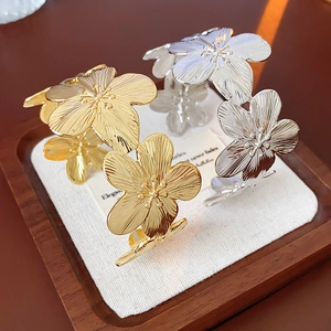 Détail de bracelets ouverts en forme de fleur dorée et argentée sur coussin en lin