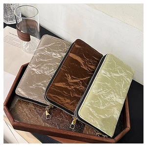 Detailed view of long zipper wallets in pleated metallic fabric on a wooden tray