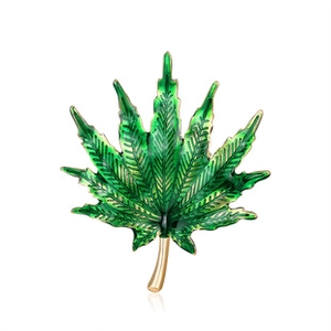 Close-up of green leaf brooch with gold edges and detailed enamel texture on white background