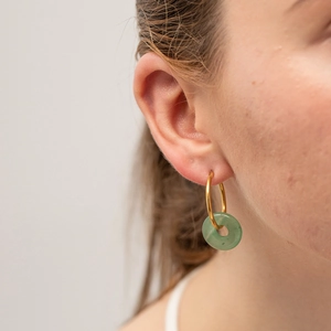 Close-up of a model wearing a gold hoop earring with a green tiger eye donut pendant