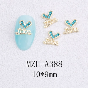 Détail de bijoux d'ongles cœur doré avec strass bleus et gravure du mot Love