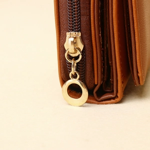 Macro detail of golden metal zipper and circular ring pull on brown leather wallet