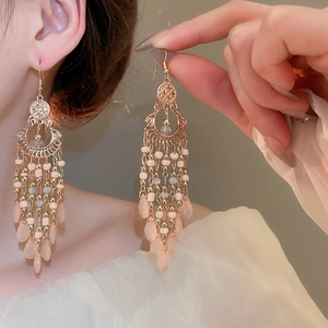 Detail of elegant gold tassel earrings with pink beads worn by a model in soft lighting
