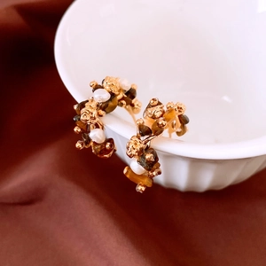 Detail view of 18K gold plated C-shaped earrings with tiger eye stone and baroque pearls