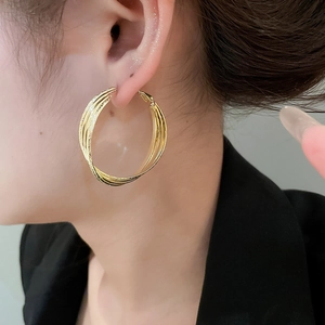 Détail d'un mannequin portant des créoles multicouches croisées plaquées or 18 carats