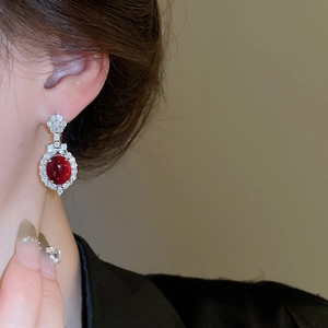 Close-up of a model wearing ruby-red oval flower stud earrings with sparkling crystals
