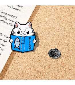 Detailed view of white enamel cat pin with blue book and metal butterfly clutch backing